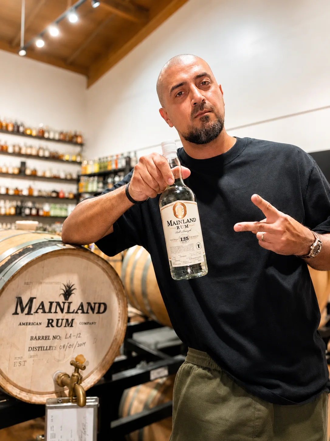 Seth Benhaim holding Mainland Still Strength rum beside an oak barrel